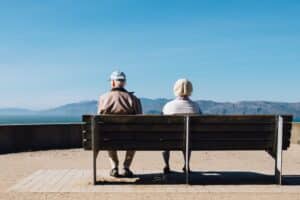 Un homme et une femme âgés, de dos, assis sur un banc et regardant un paysage de montagne
